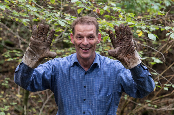 Eine Person, welche an einem Natureinsatz teilnimmt, streckt die erdigen Gartenhandschuhe in die Höhe.