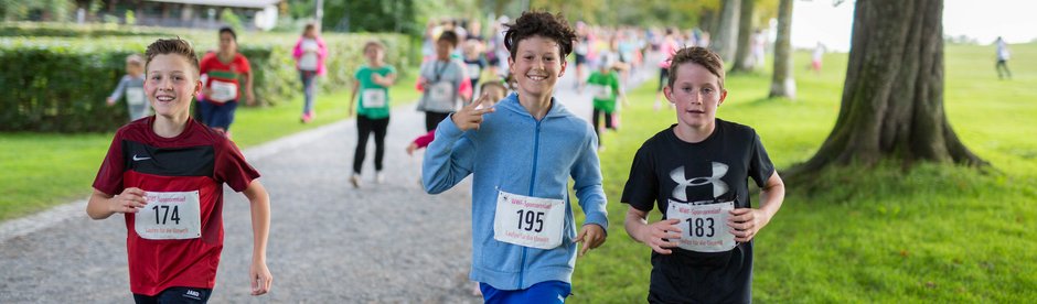 WWF Läufe im Sportunterricht oder am Sporttag Drei Kinder, die an einem Lauf teilnehmen und joggend in die Kamera lächeln.